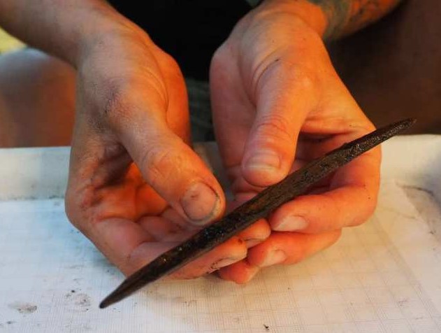 Alisha Gauvreau sostiene un artefacto tallado en madera con dos puntas de 7.000 años de antigüedad. Este artefacto podría haber sido utilizado como anzuelo para capturar peces.