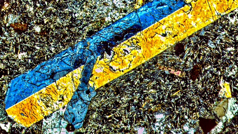 En un corte microscópico polarizado cruzado de una muestra de núcleo, el cristal azul y amarillo que puede verse es titanio-augita, rodeado por una masa de minerales del suelo, que incluyen feldespatos, flogopita, espinela, perovskita y apatita. Este conjunto sugiere que la fuente del manto, rica en agua, produjo esta lava