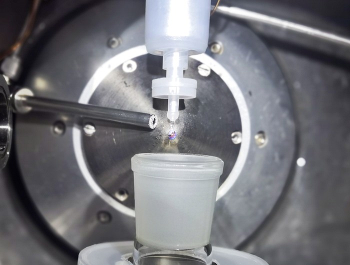 En la cámara de muestras, la aleación NaK gotea de una boquilla. A medida que crece la gota, el vapor de agua fluye hacia la cámara de muestra y forma una capa delgada en la superficie de la gota