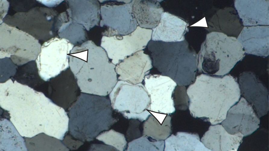 Imagen de microscopio de la muestra de sarsen que muestra el mosaico de cristales de cuarzo estrechamente entrelazados que unen la roca. Los contornos de los granos de arena de cuarzo se indican con flechas