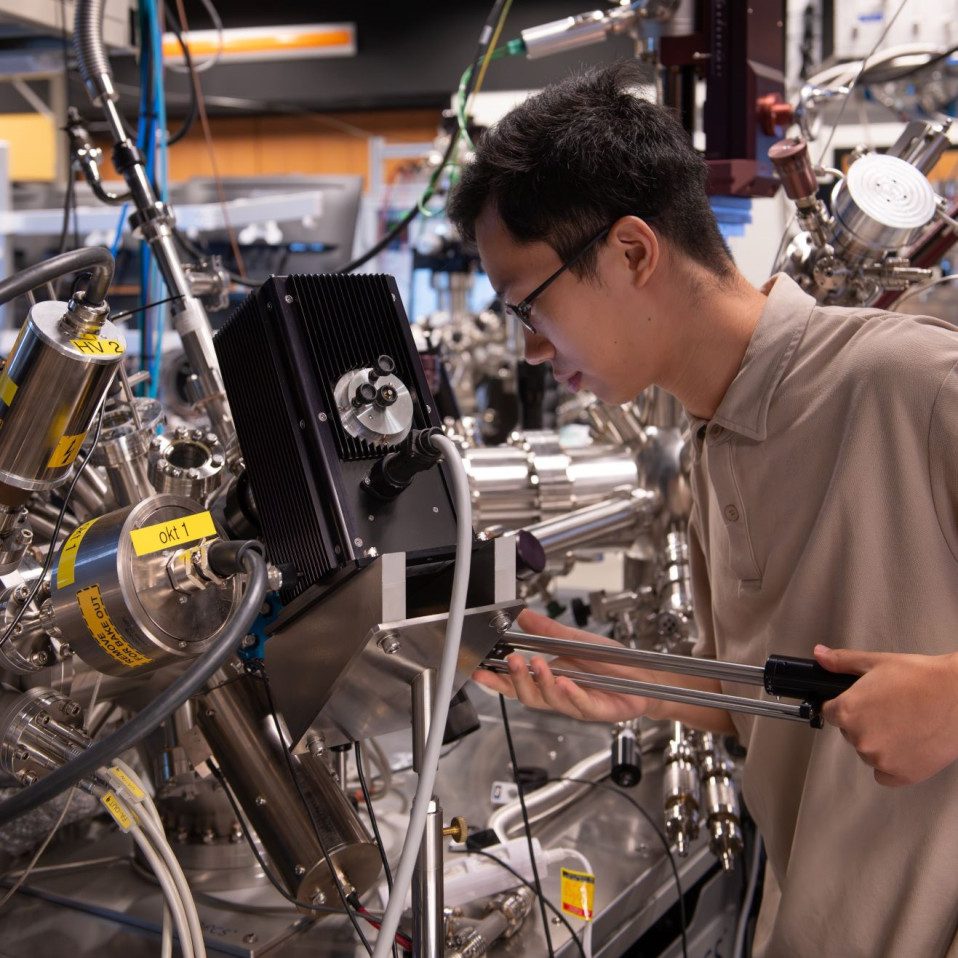 La configuración de espectroscopia de fotoemisión resuelta en tiempo y ángulo (TR-ARPES) en el OIST, aquí con el coautor principal del estudio, Xing Zhu, estudiante de doctorado de la Unidad de Espectroscopia Femtosegundo. Con una fuente de ultravioleta extrema de mesa patentada que emite ráfagas a intervalos de femtosegundos (1 fs = una millonésima parte de una milmillonésima parte de un segundo), esta configuración capturó las primeras imágenes reales de excitones, ayudó a esbozar la evolución de los excitones oscuros y ahora ha demostrado la viabilidad de la ingeniería excitonica de Floquet.